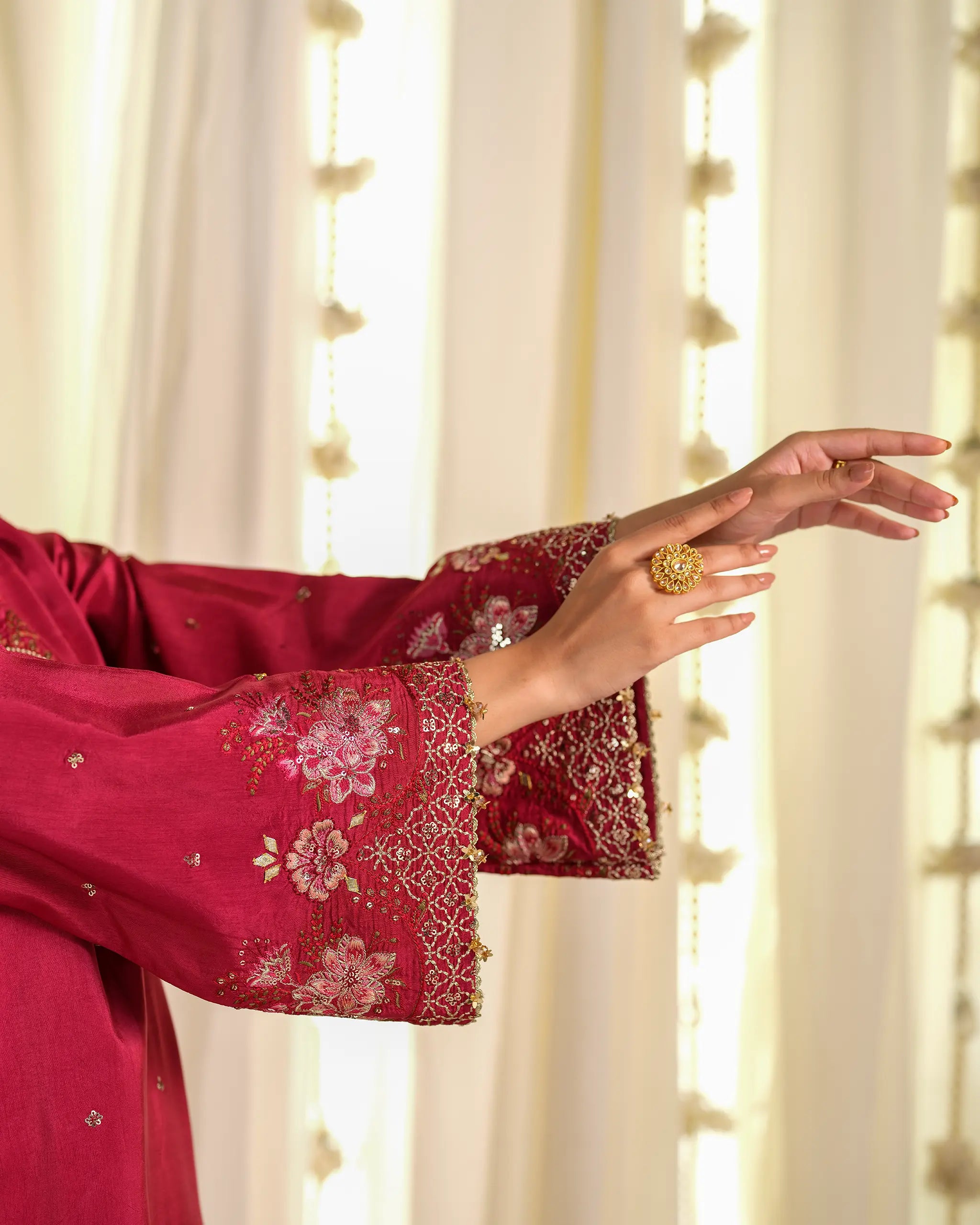 Detailed close-up of the sleeve on the 'Chahat﻿' suit, showcasing intricate pink floral embroidery, beadwork, and a statement gold ring.