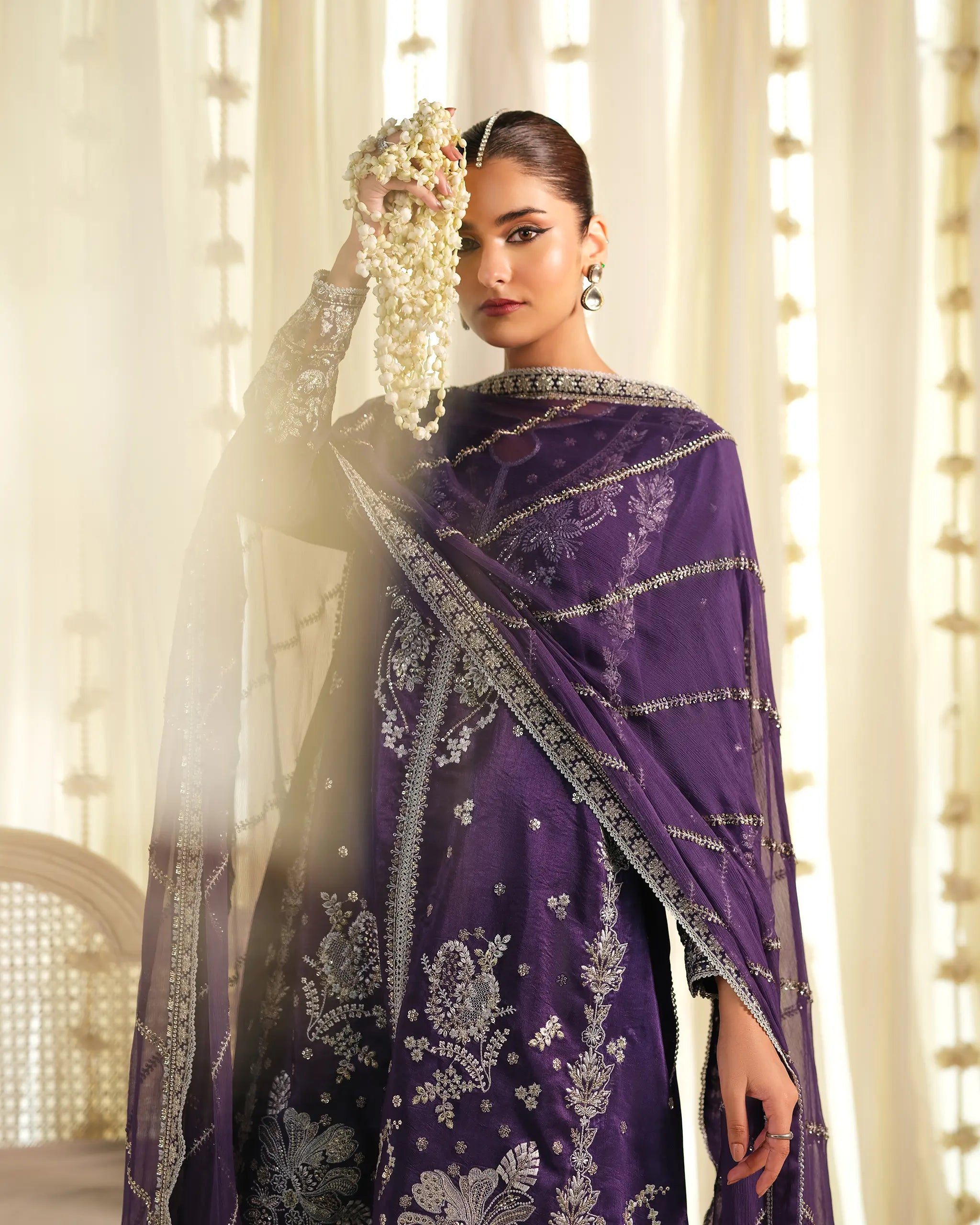 A close-up shot of a model holding a jasmine garland, wearing the embroidered purple 'Khumaar﻿' kameez and a sheer 'dupatta﻿' from the 'Pehla Khat﻿' collection.