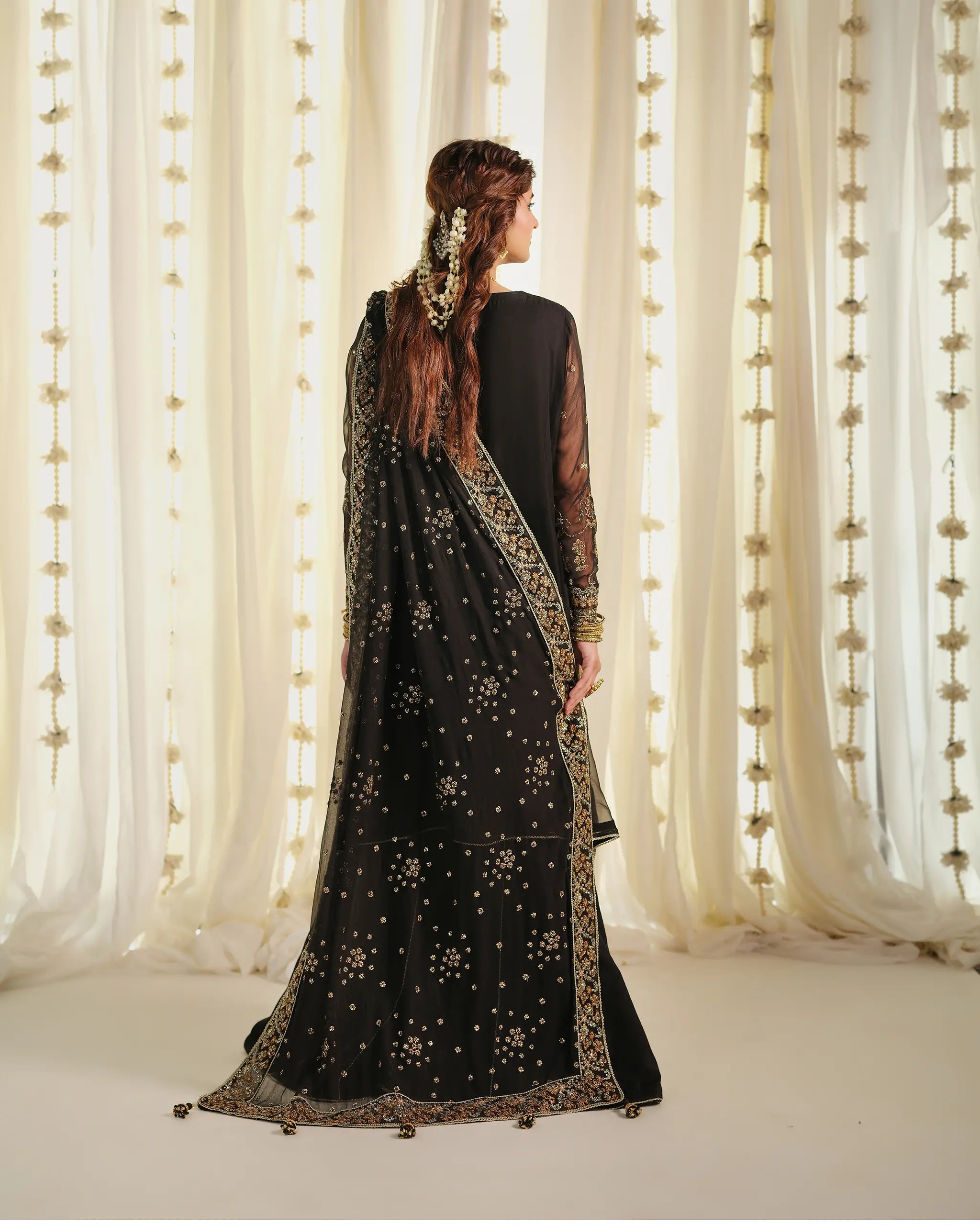Back view of the black 'Mahtaab﻿' dress, showcasing the heavily embroidered organza dupatta﻿ with scatter motifs and detailed border, paired with a traditional hair accessory.