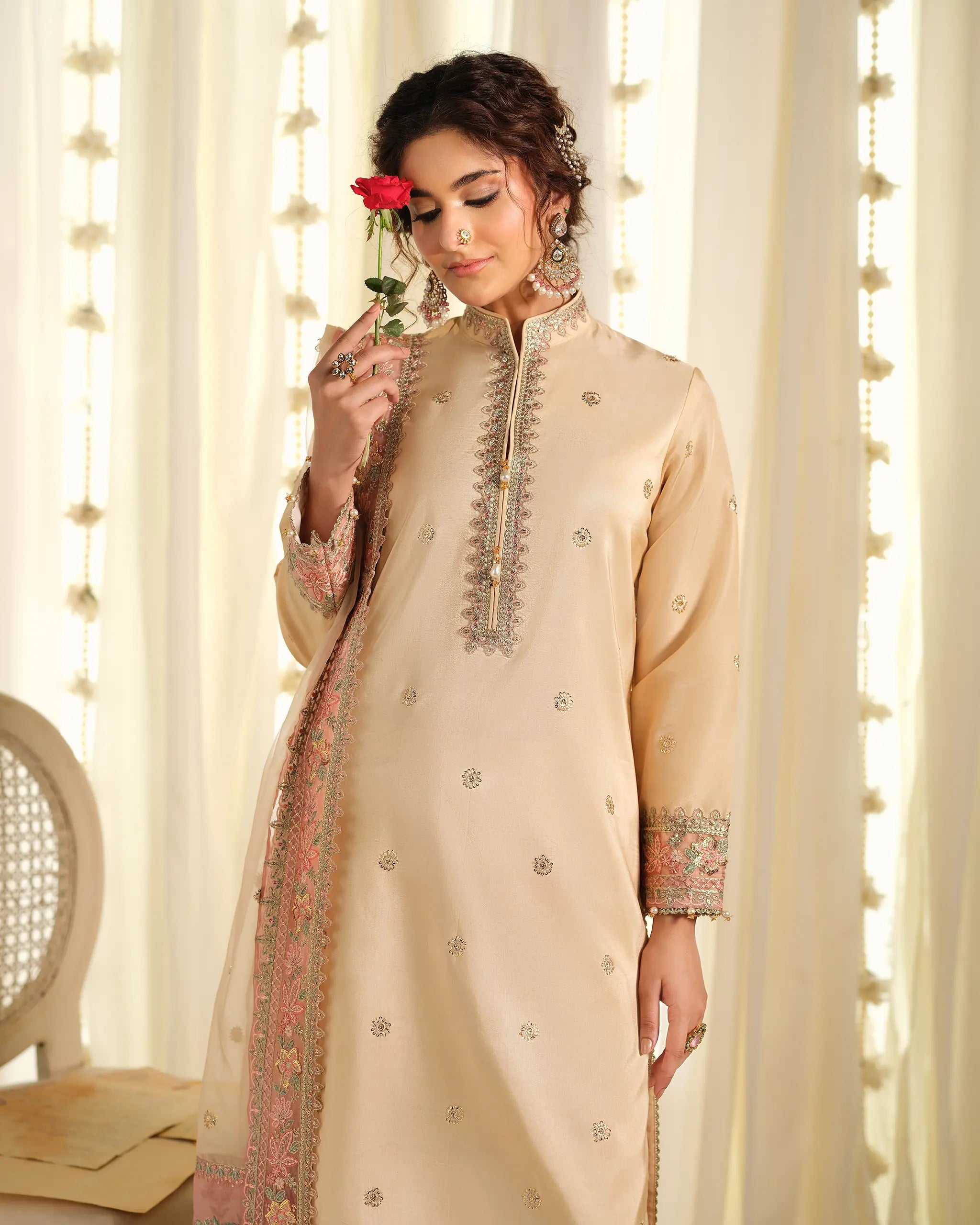 Close-up of a model smelling with a red rose while wearing the beige 'Tehreer﻿' suit, highlighting the neckline embroidery and elegant styling.