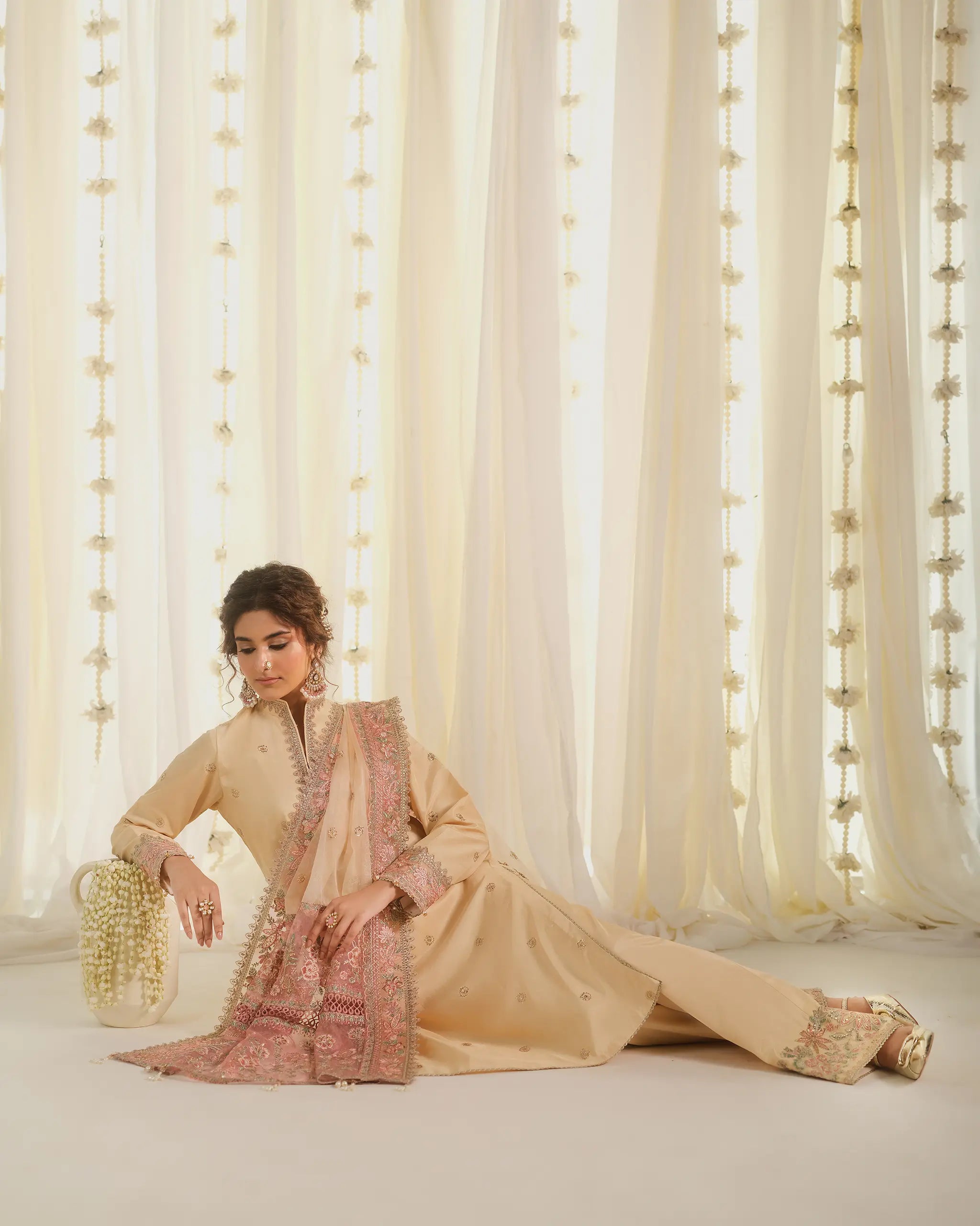 Model reclining gracefully in a beige raw silk outfit 'Tehreer' with a pink embroidered dupatta﻿, from the 'Pehla Khat﻿' festive collection by Sinoor.