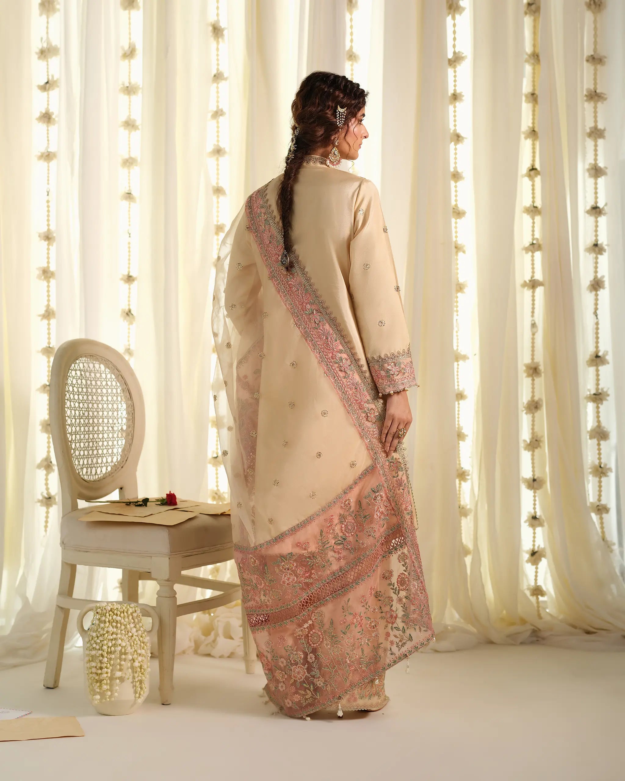 The back view of the beige 'Tehreer﻿' outfit, showcasing the elegant drape of the sheer pink embroidered dupatta﻿ and a braided hairstyle.