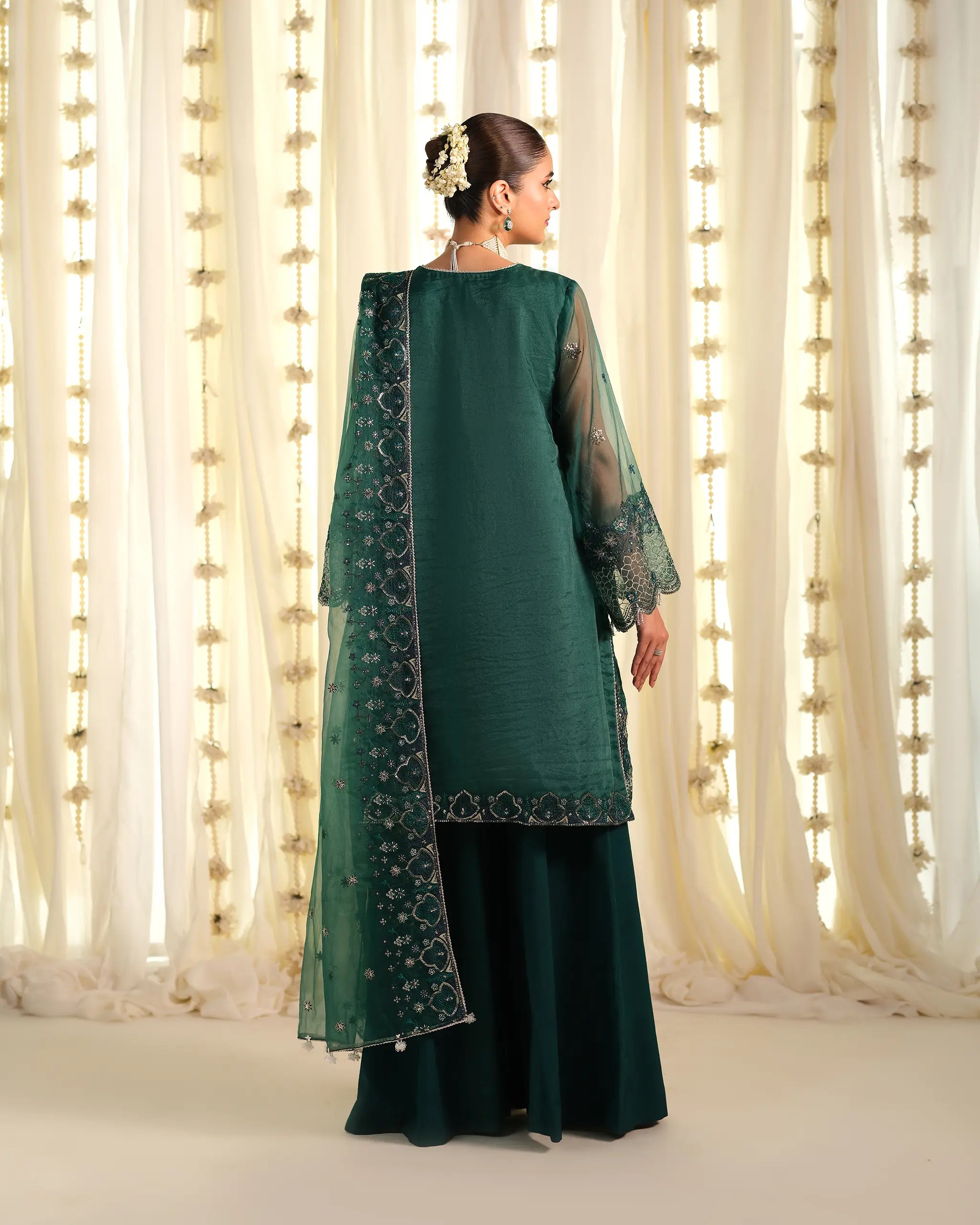The back view of the green 'Pehla Khat Vasl﻿' outfit, showing the sheer organza dupatta﻿ with detailed border embroidery and a floral hair accessory.