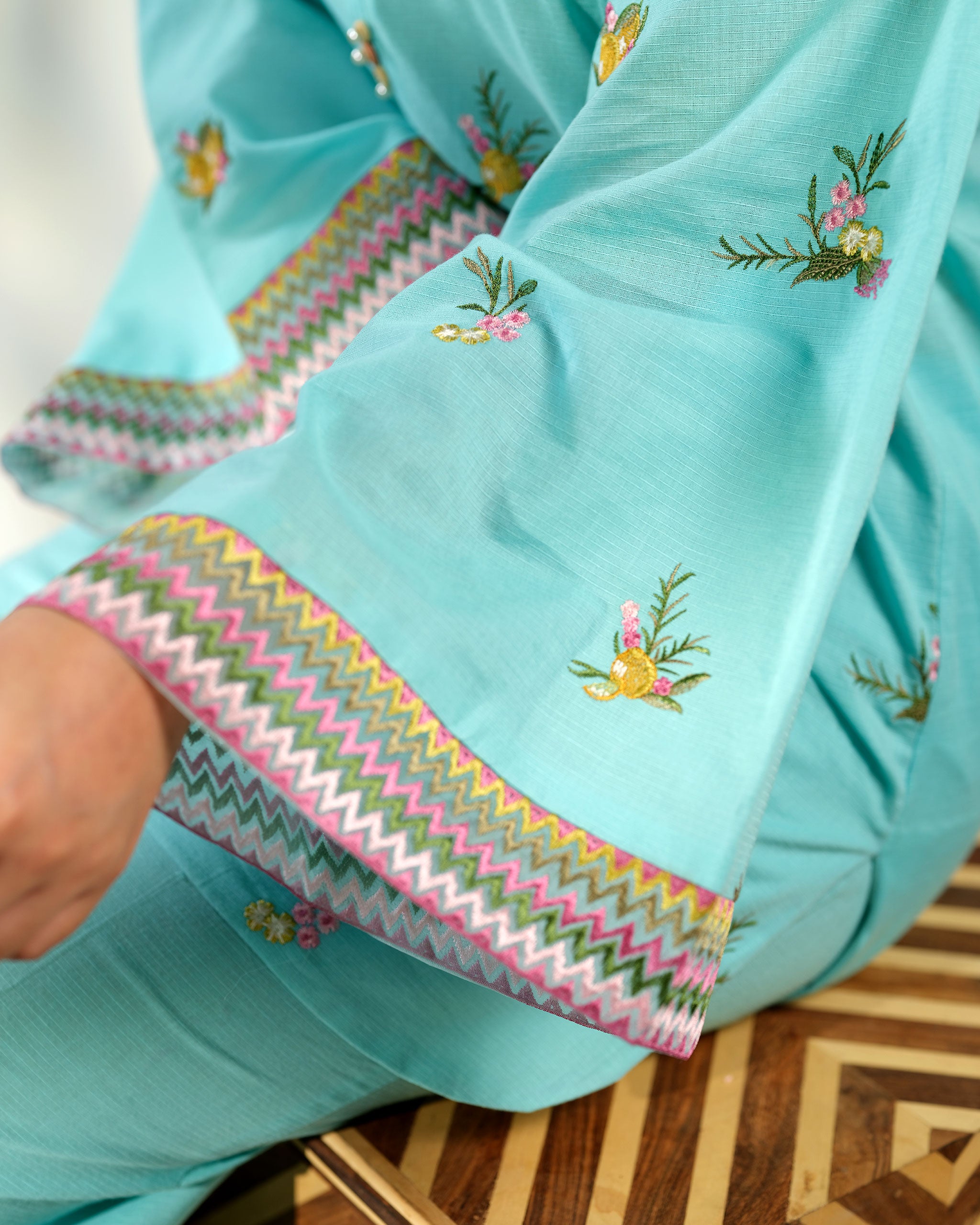 Sinoor Shop pret casual 2025 Amal Light Blue outfit. A woman models a light blue kurta and trousers while seated. The long-sleeved kurta has delicate floral embroidery and patterned cuffs. Soft studio lighting.