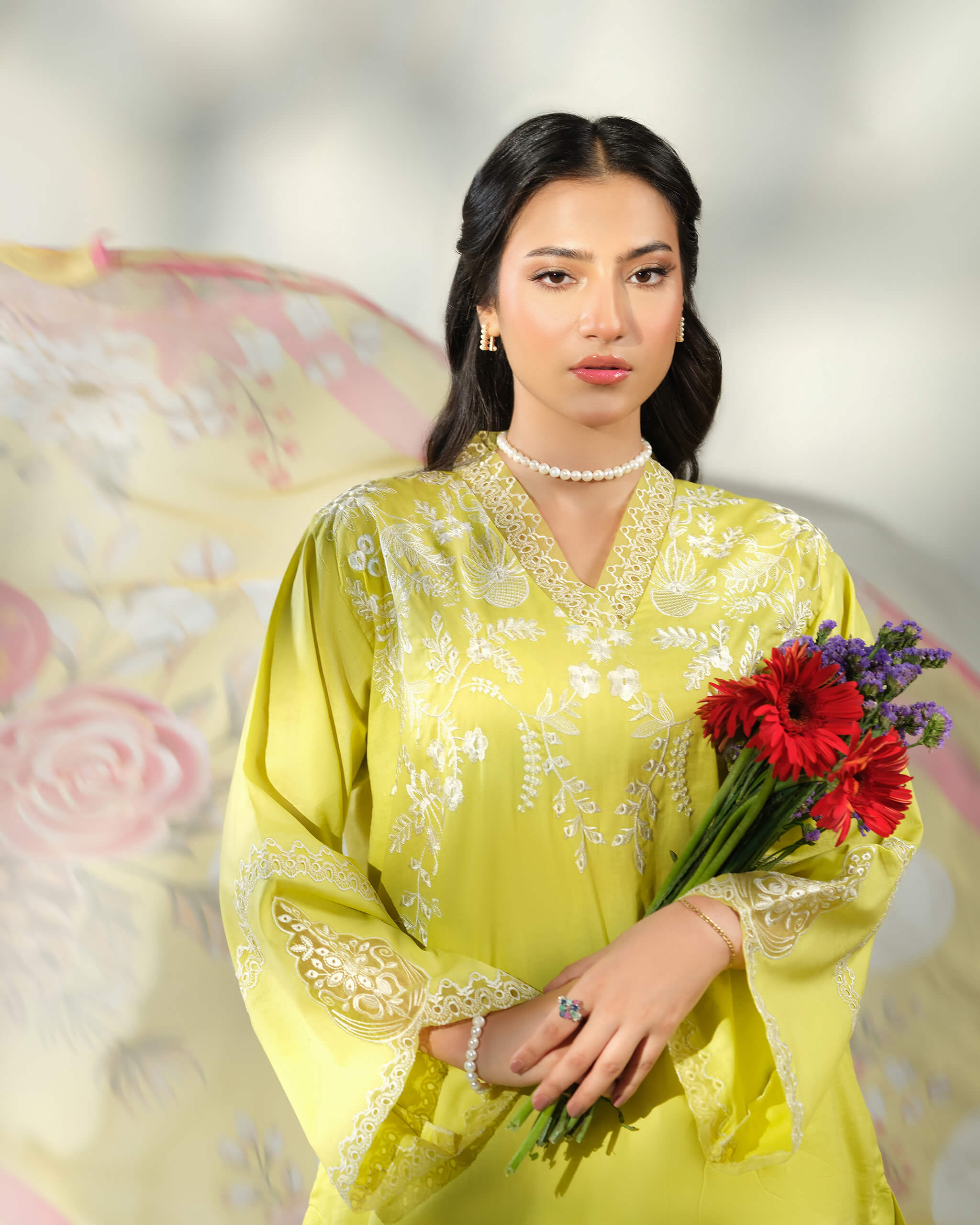 Sinoor Shop pret casual 2025 Asra Lime Yellow outfit. A woman wearing a lime yellow embroidered kurta and a pearl necklace holds a bouquet of red gerbera daisies and purple flowers. A floral dupatta is partially visible in the background. Close-up shot, soft lighting.