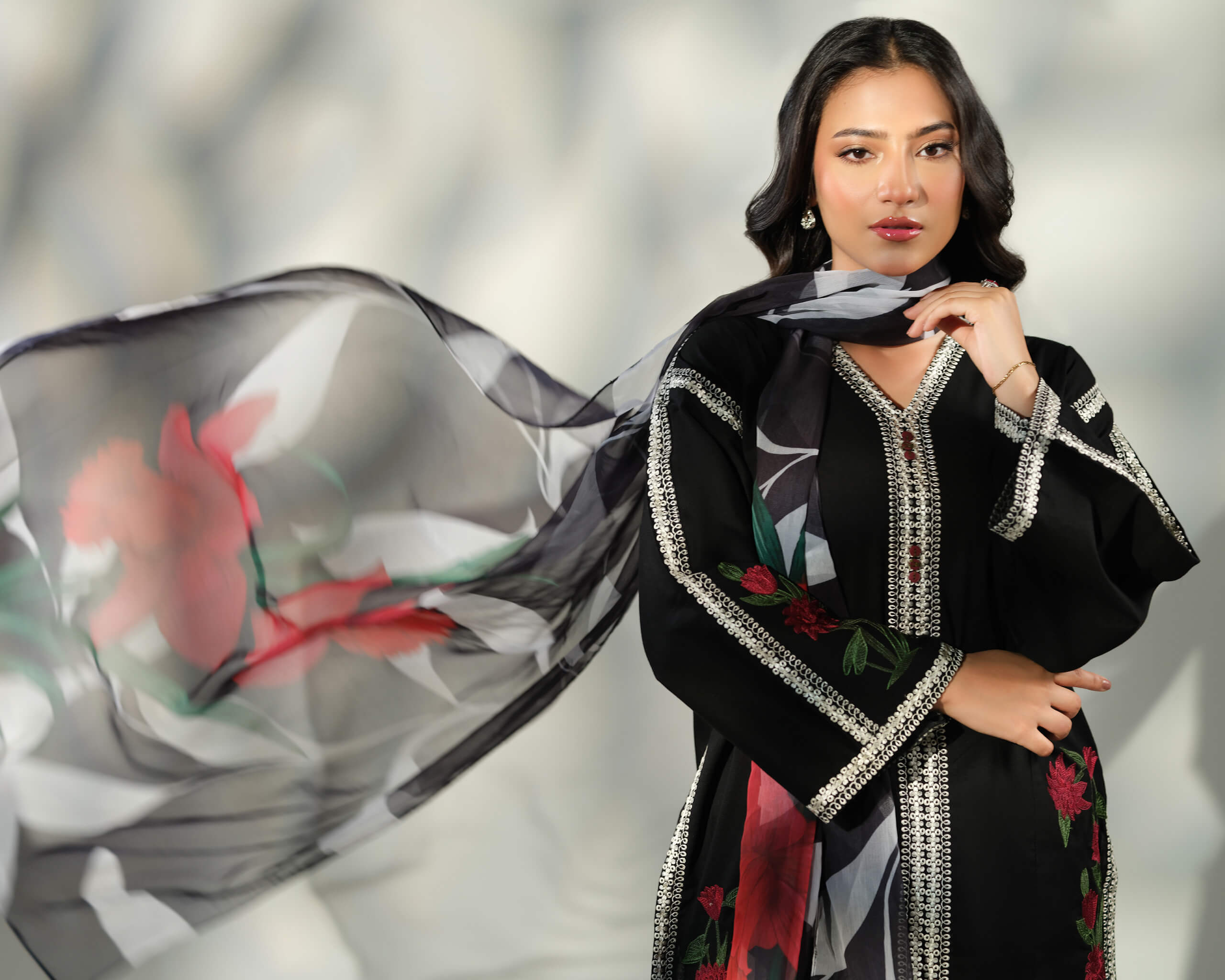 Sinoor Shop pret casual 2025 Ayzel Black outfit. A woman models a black embroidered kurta with a flowing floral printed dupatta. She has dark hair and is wearing delicate jewelry. Studio shot with dynamic lighting highlighting the dupatta's movement.