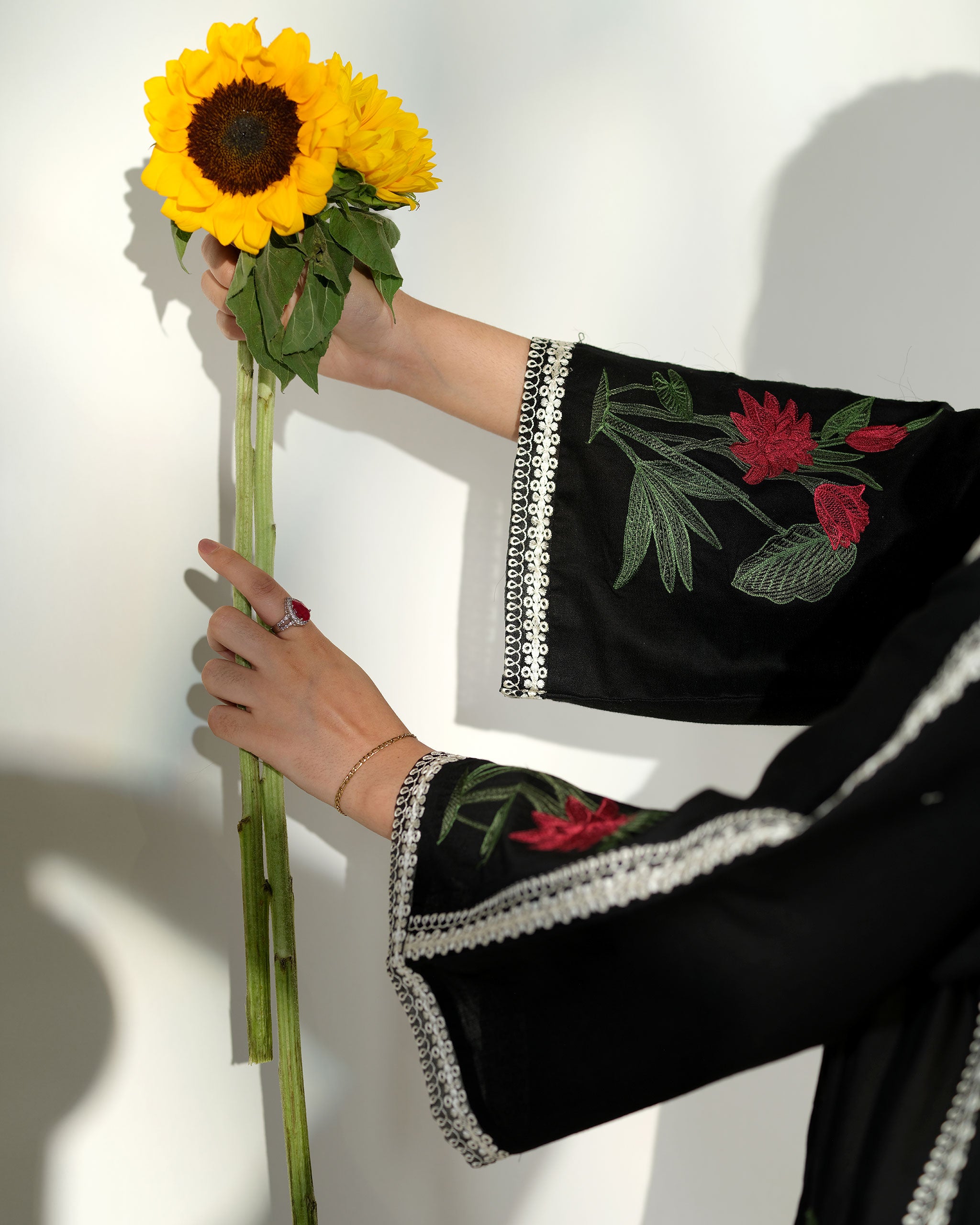 Sinoor Shop pret casual 2025 Ayzel Black outfit. A woman walks, a large black and white floral dupatta flowing behind her. She wears a black embroidered kurta and trousers, paired with embellished heels. Full-length shot, dynamic studio lighting with shadows.