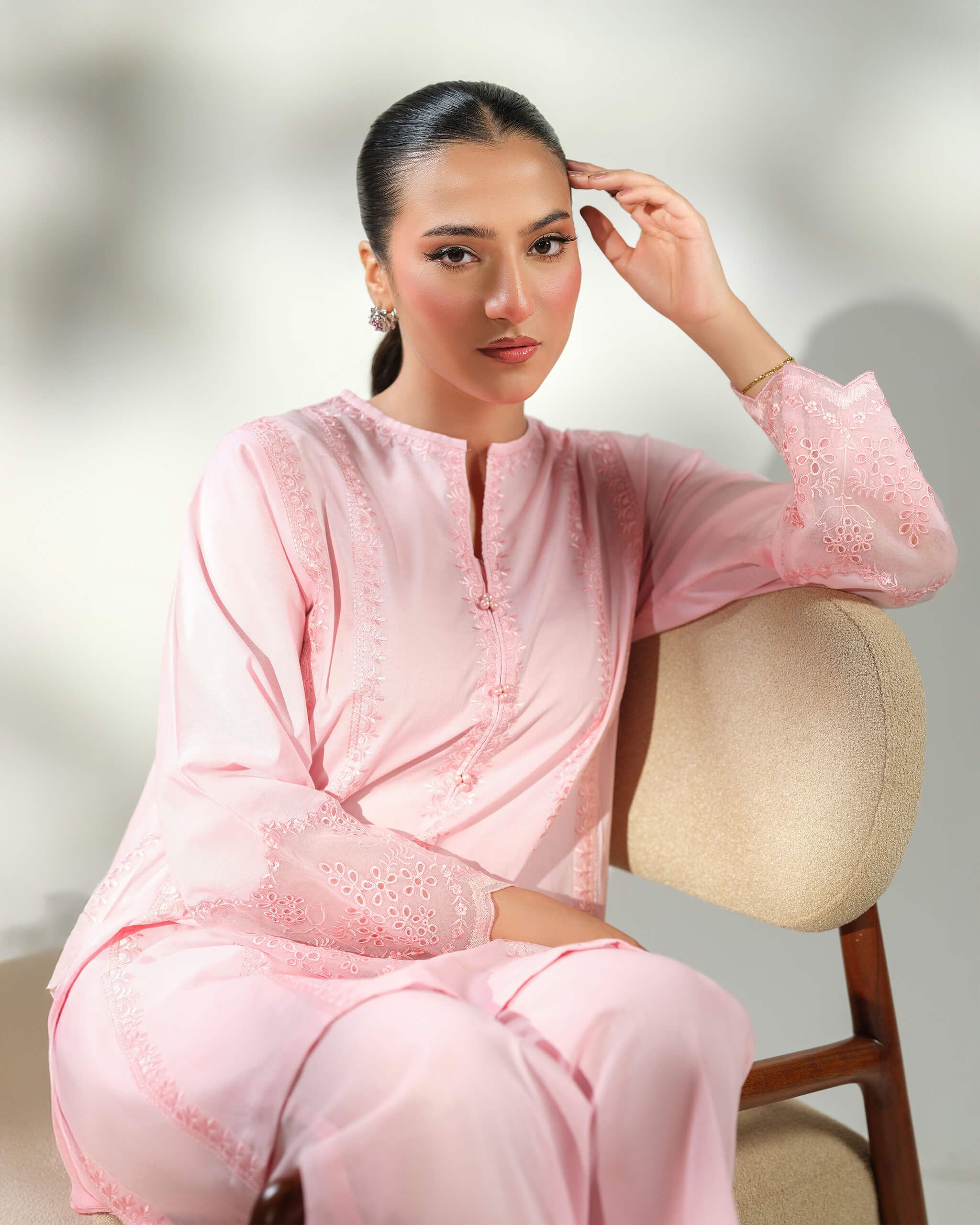Sinoor Shop pret casual 2025 Mira Baby Pink outfit. A woman with dark hair pulled back is seated, wearing a light baby pink kurta and trousers. The kurta has intricate white embroidery on the sleeves. She is wearing delicate jewelry. Seated pose, soft studio lighting.