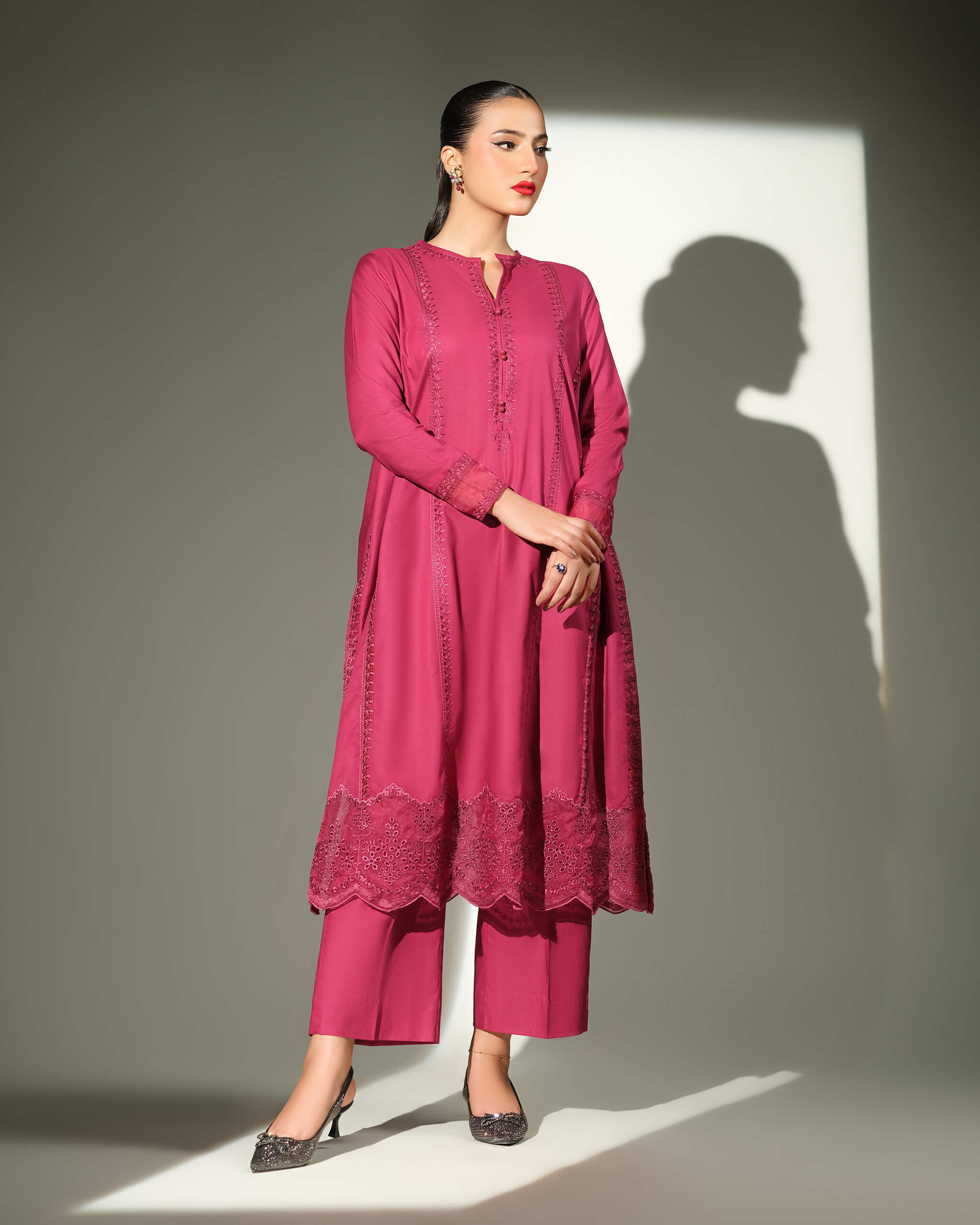 Sinoor Shop pret casual 2025 Sible Dark Pink outfit. A woman stands in a dark pink embroidered kurta and matching straight trousers. She has dark hair pulled back, red lipstick, and is wearing embellished black heels. Full-length shot, studio lighting with a defined shadow.